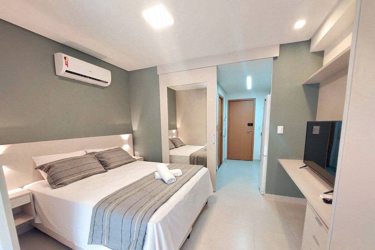Una habitación de hotel moderna con una cama grande, mesitas de noche, un equipo de aire acondicionado, un televisor y un espejo.