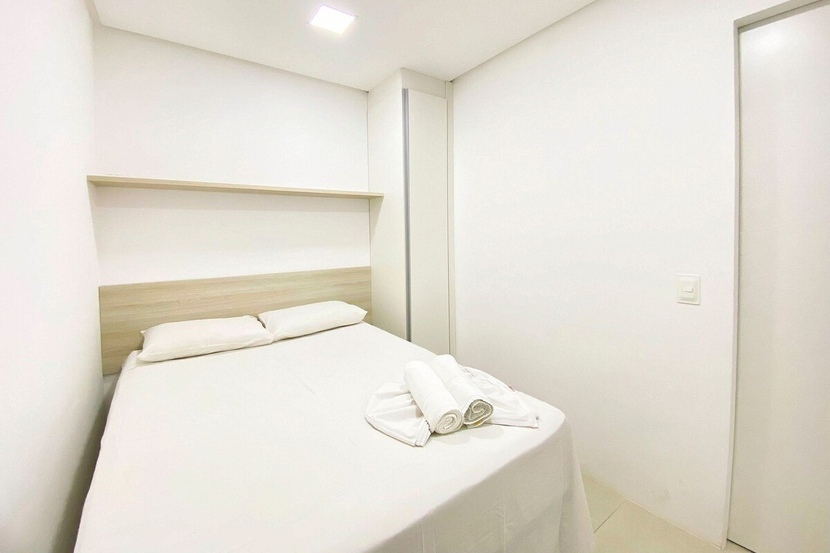 A modern hotel room with a bed, a wooden headboard, a white wall, and a door.