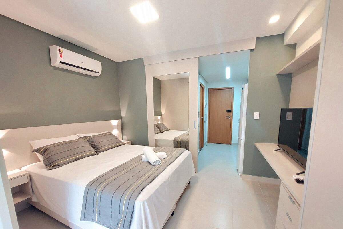 A modern hotel room with a large bed, bedside tables, an air conditioning unit, a television, and a mirror.