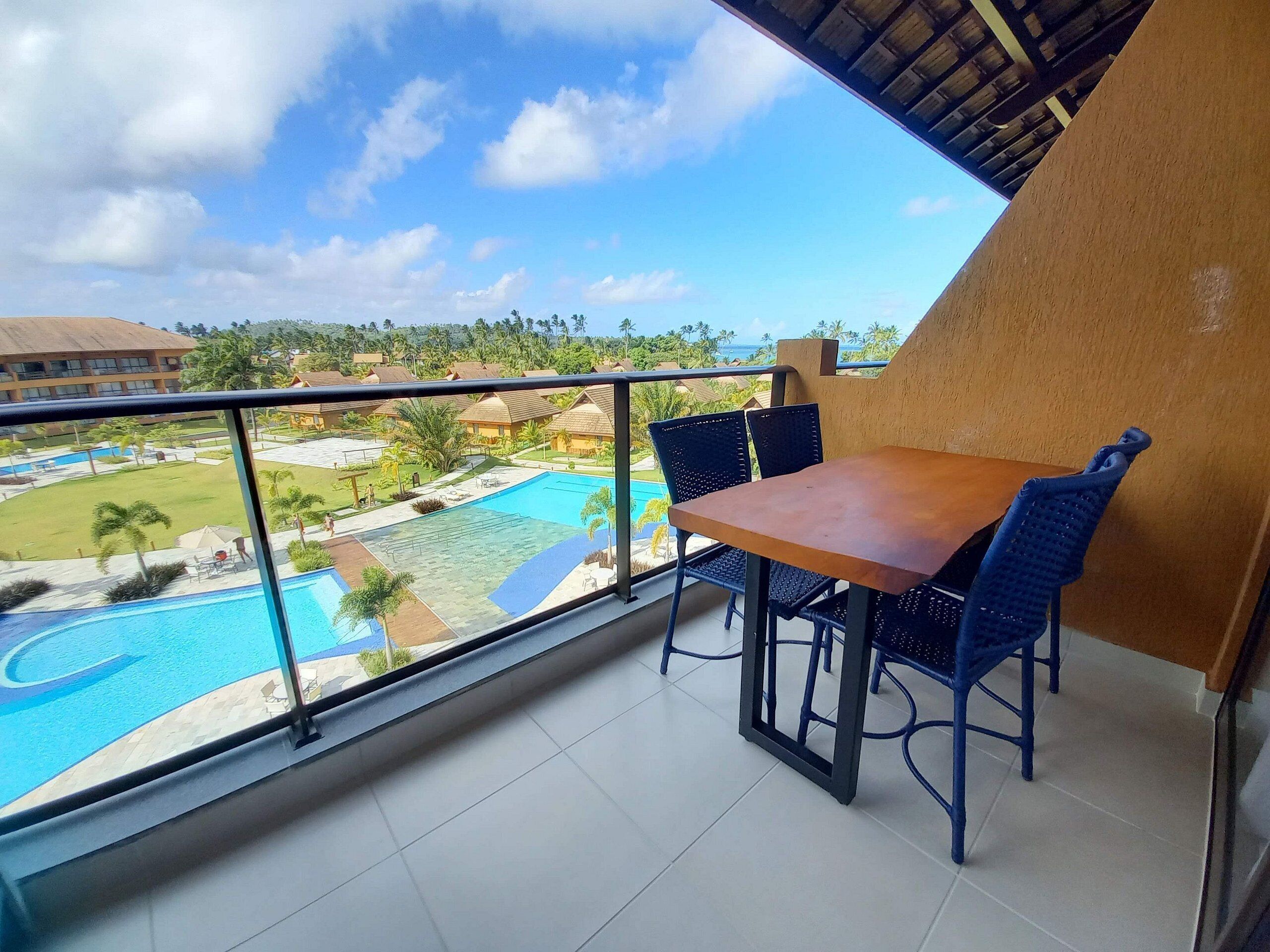 Un balcón con mesa y sillas, con vista a una piscina y edificios de un complejo turístico.