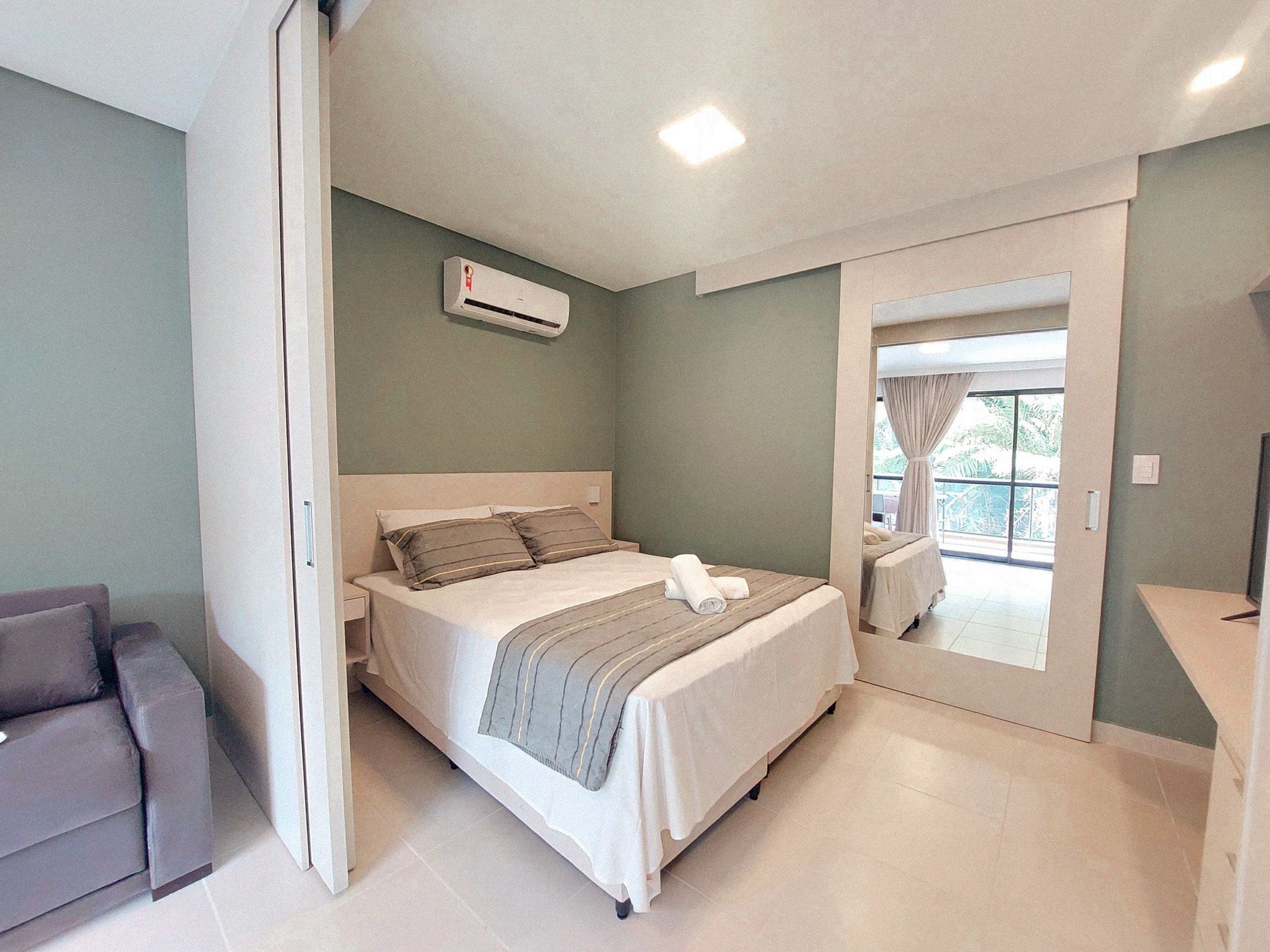 Un dormitorio con cama, sofá, balcón y aire acondicionado.