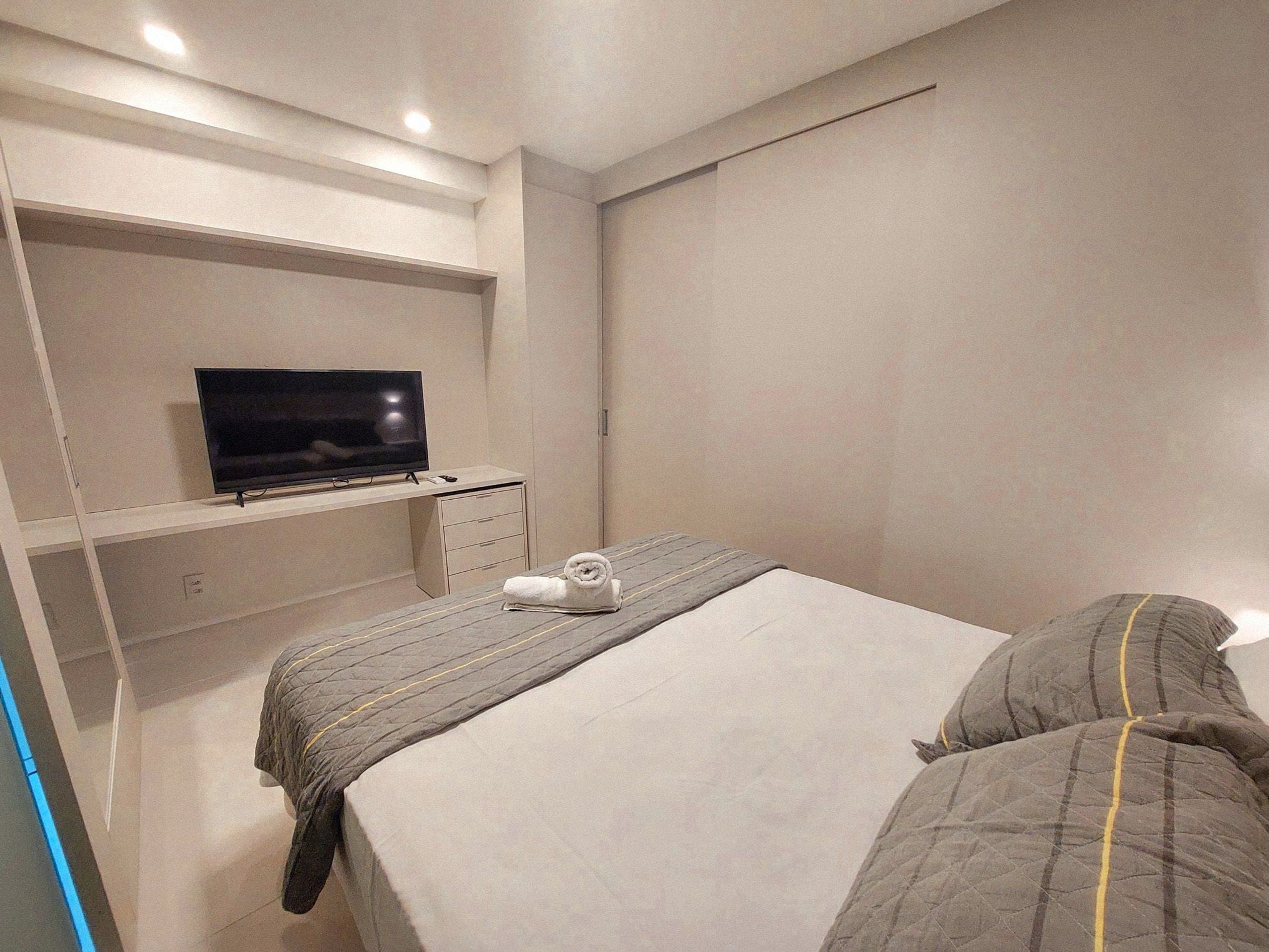 A bedroom with a bed, a TV on a shelf, and a towel on the bed.