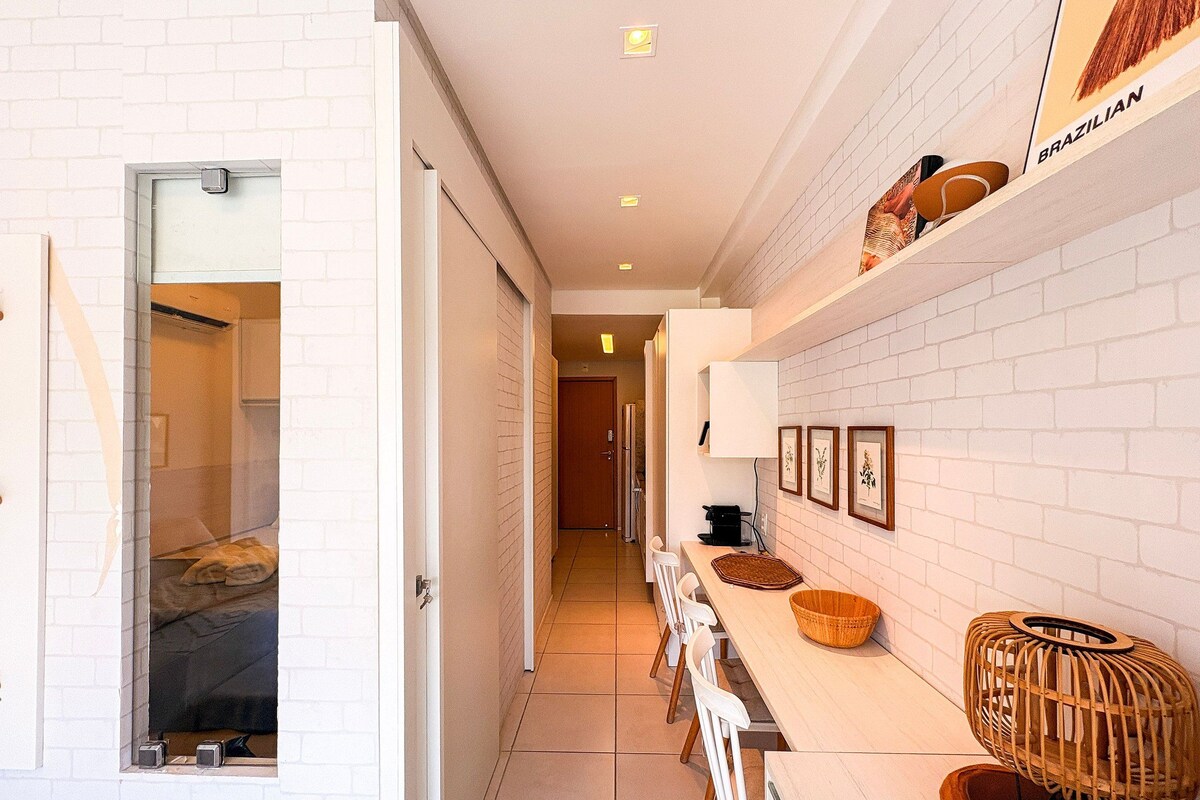 A hallway with a white brick wall, a wooden bench, a basket, and a wall-mounted shelf with items labeled 'BRZILIAN.'