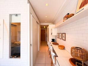 Un pasillo con pared de ladrillo blanco, un banco de madera, una cesta y un estante en la pared con artículos etiquetados 'BRZILIAN'.