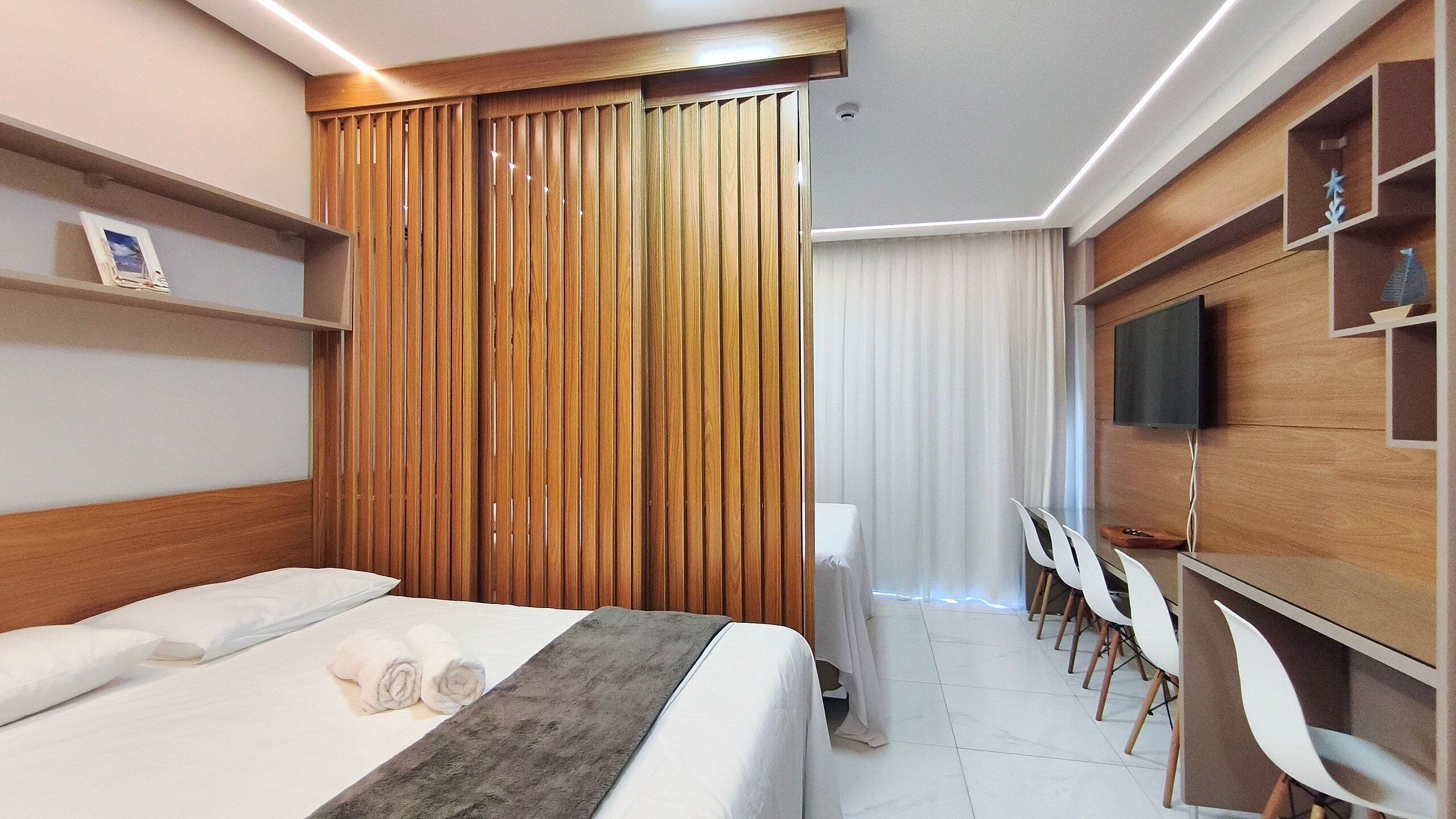 A modern hotel room with a bed, a desk, a TV, and a seating area.