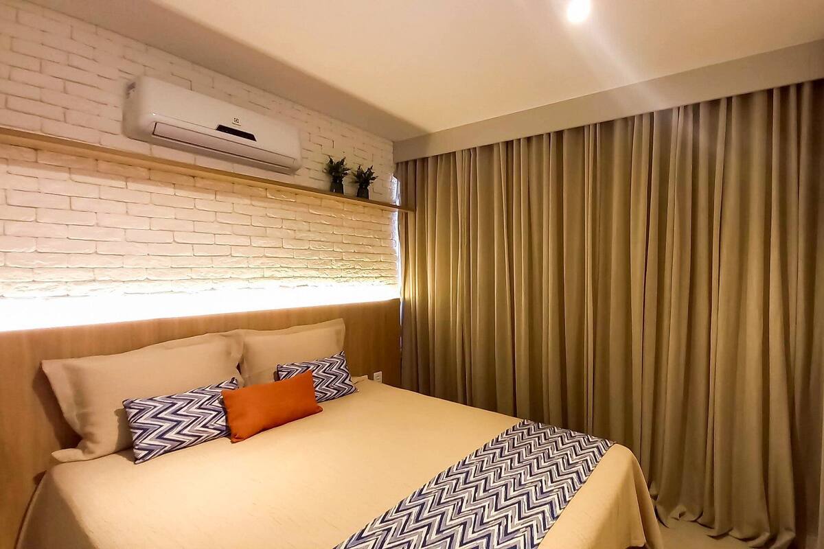 Habitación de hotel con cabecera de ladrillo, cama con ropa de cama estampada, televisor de pantalla plana y ventana con cortinas.
