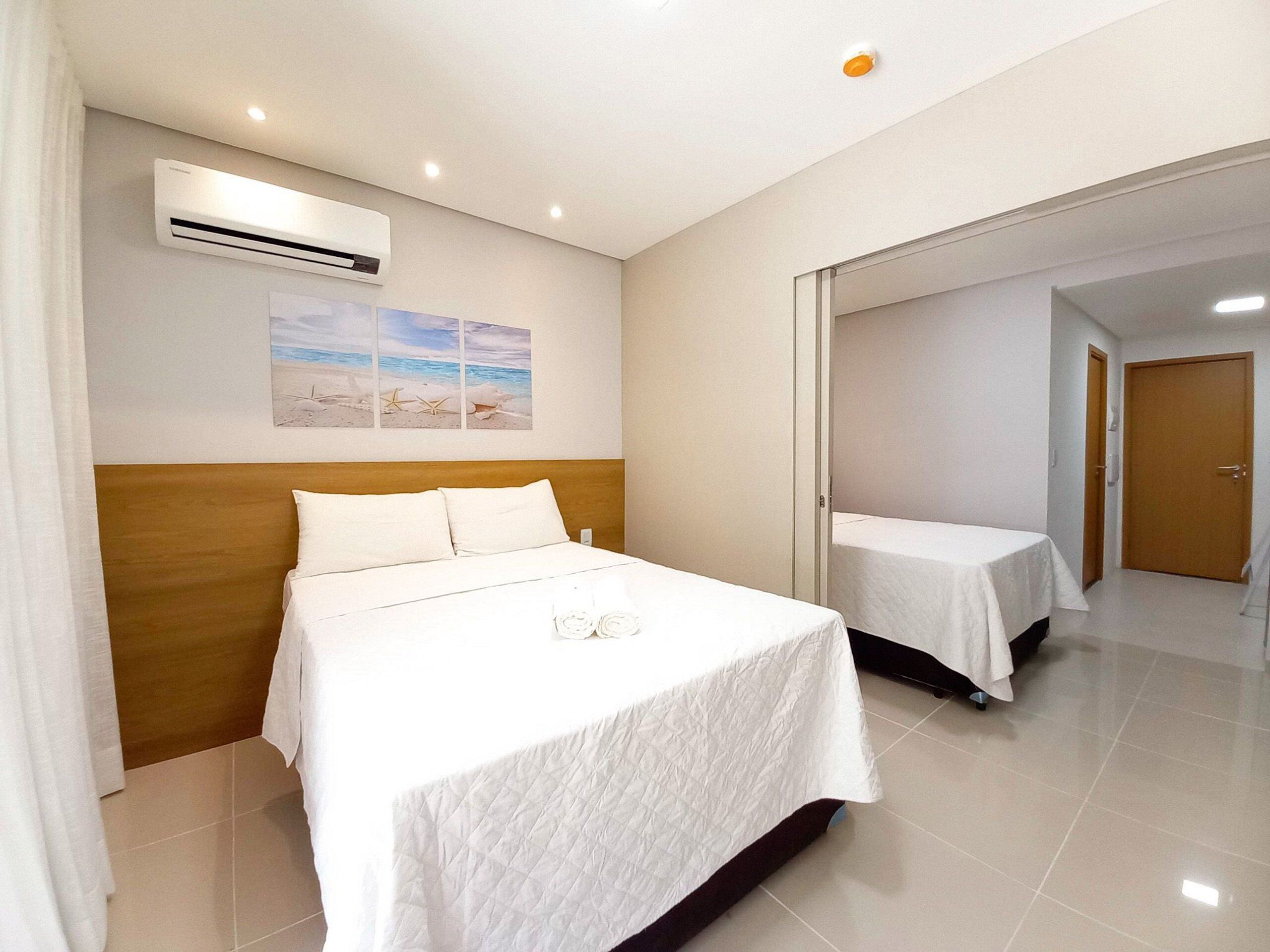 A hotel room with a bed, a wall-mounted air conditioner, and a beach-themed picture.