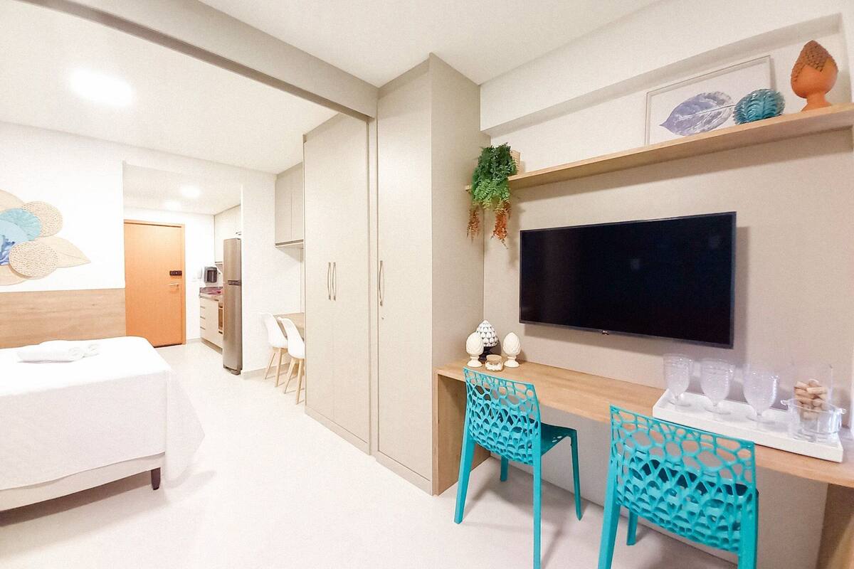 Una habitación de hotel moderna con una cama, un escritorio con dos sillas, un televisor y un pequeño estante con objetos decorativos.