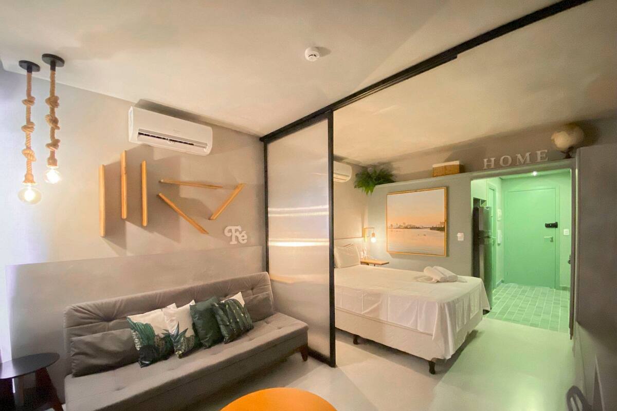 Un dormitorio moderno con una cama, un sofá y un pequeño taburete naranja.