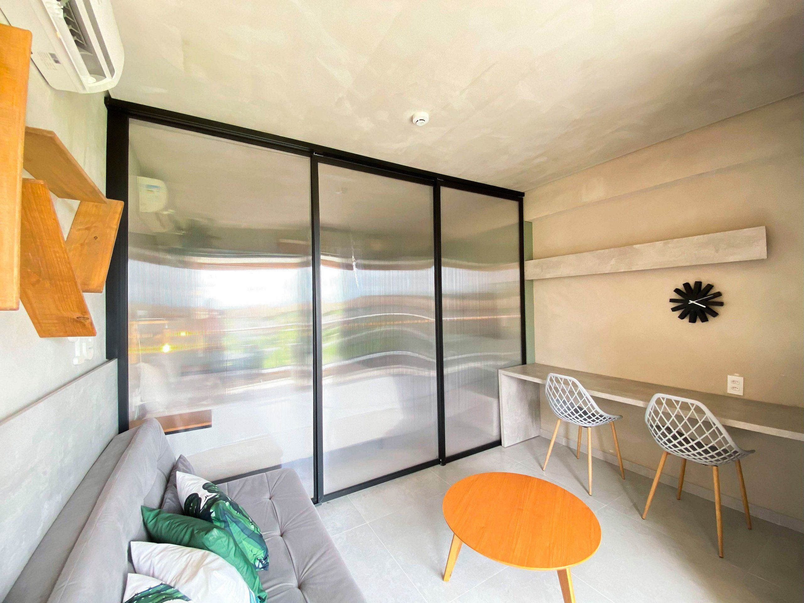 Een moderne woonkamer met een bank, een ronde houten tafel, twee stoelen, een grote schuifdeur met glas en een wandklok.