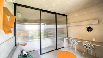Een moderne woonkamer met een bank, een ronde houten tafel, twee stoelen, een grote schuifdeur met glas en een wandklok.