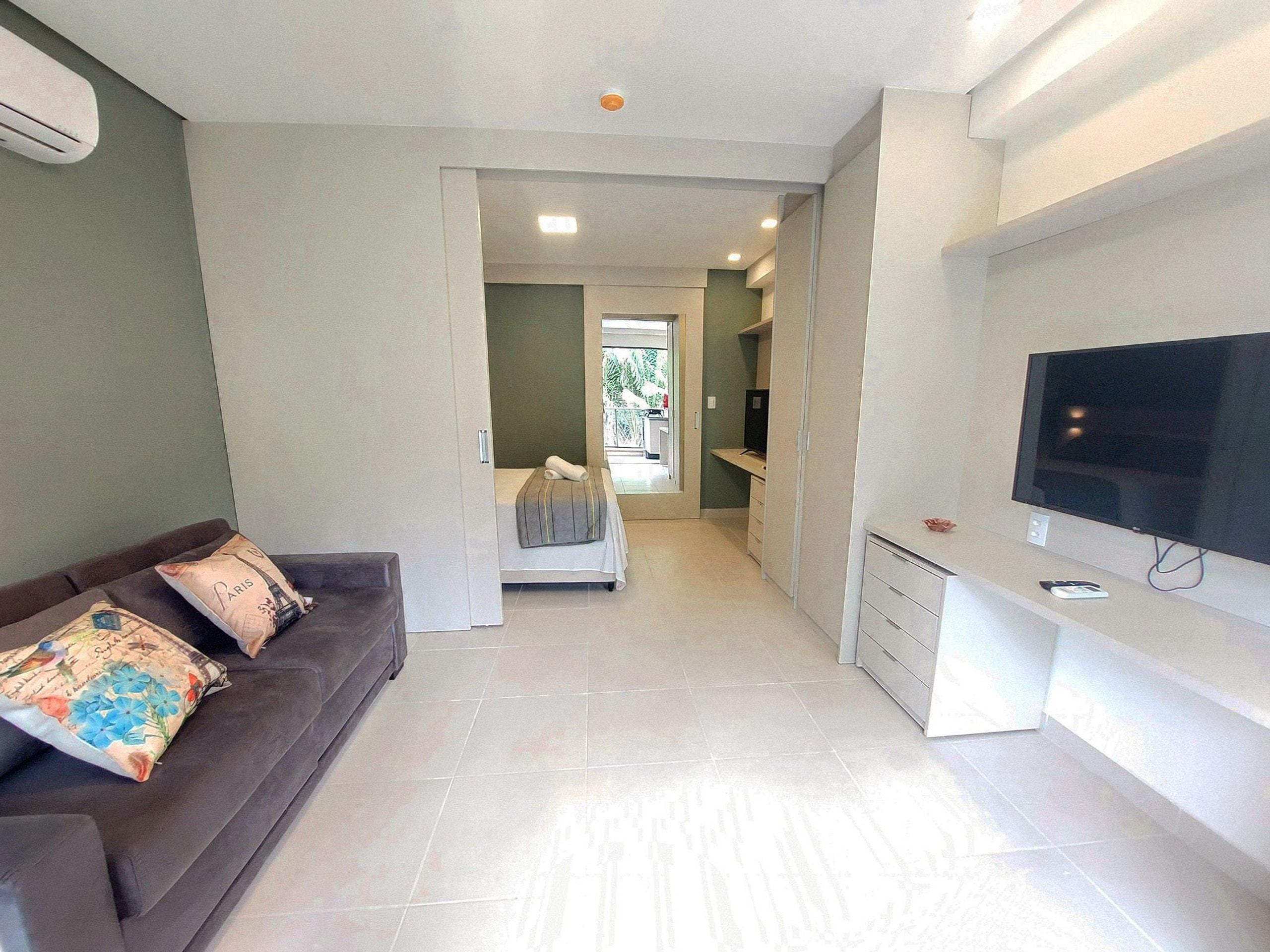 A modern living room with a sofa, a flat-screen TV, and a hallway leading to a bedroom.