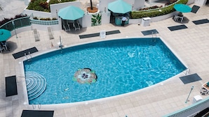 A rectangular swimming pool with a central island, surrounded by lounge chairs and umbrellas. - Waikiki Condo - Ocean View - Minutes from the Beach! (Honolulu)