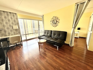 Relax in this stylish living room with a large window offering a view of the city, a comfortable sofa, and a desk for work.