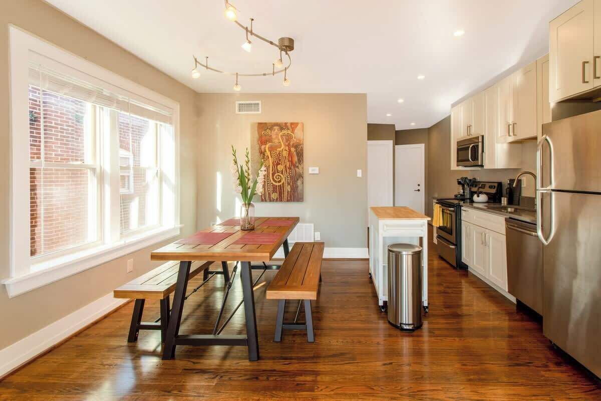 Een moderne keuken met houten vloeren, een eettafel met banken, een roestvrijstalen koelkast en een magnetron.