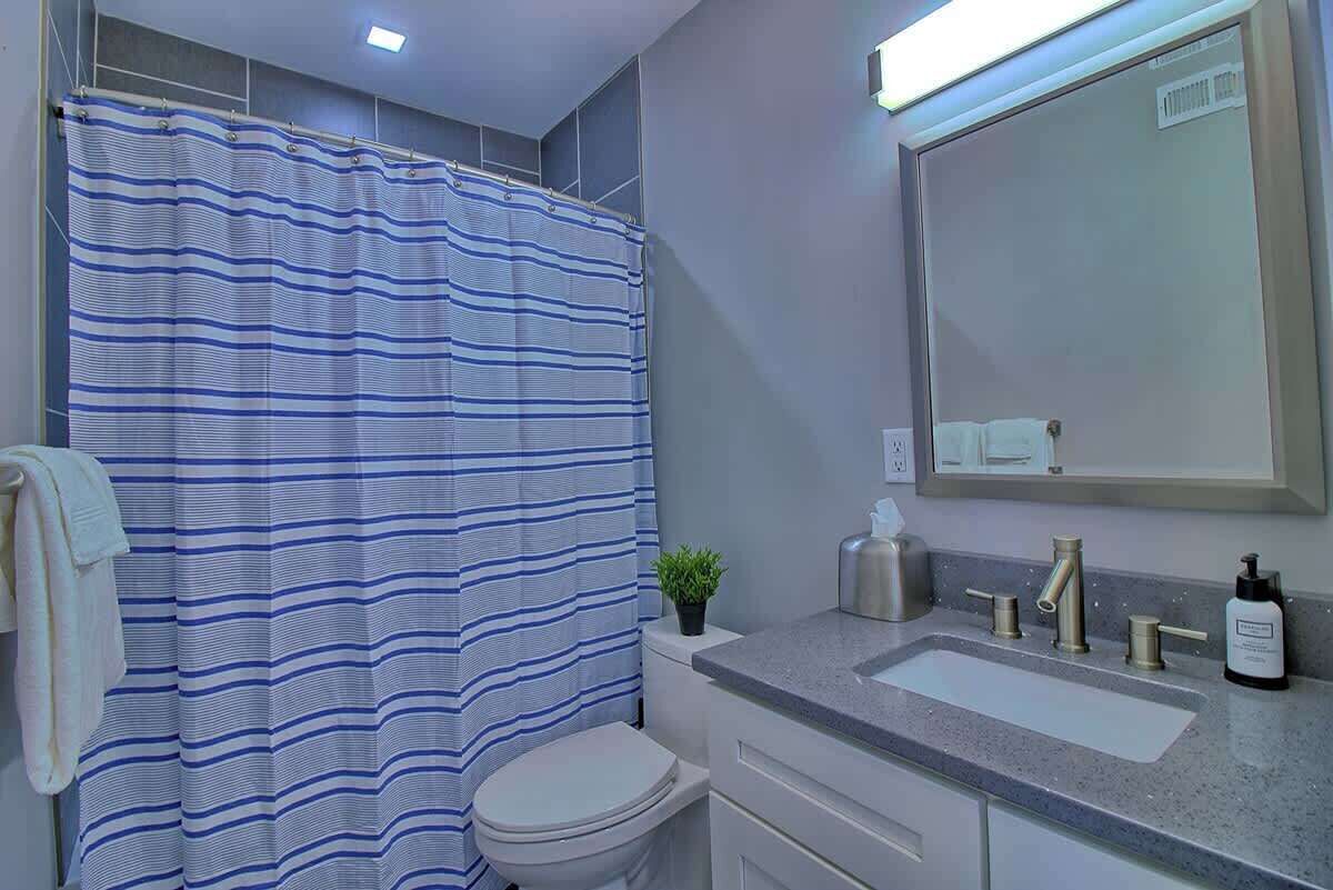 Un baño con cortina de ducha a rayas, inodoro, lavabo con espejo y una pequeña planta en maceta.