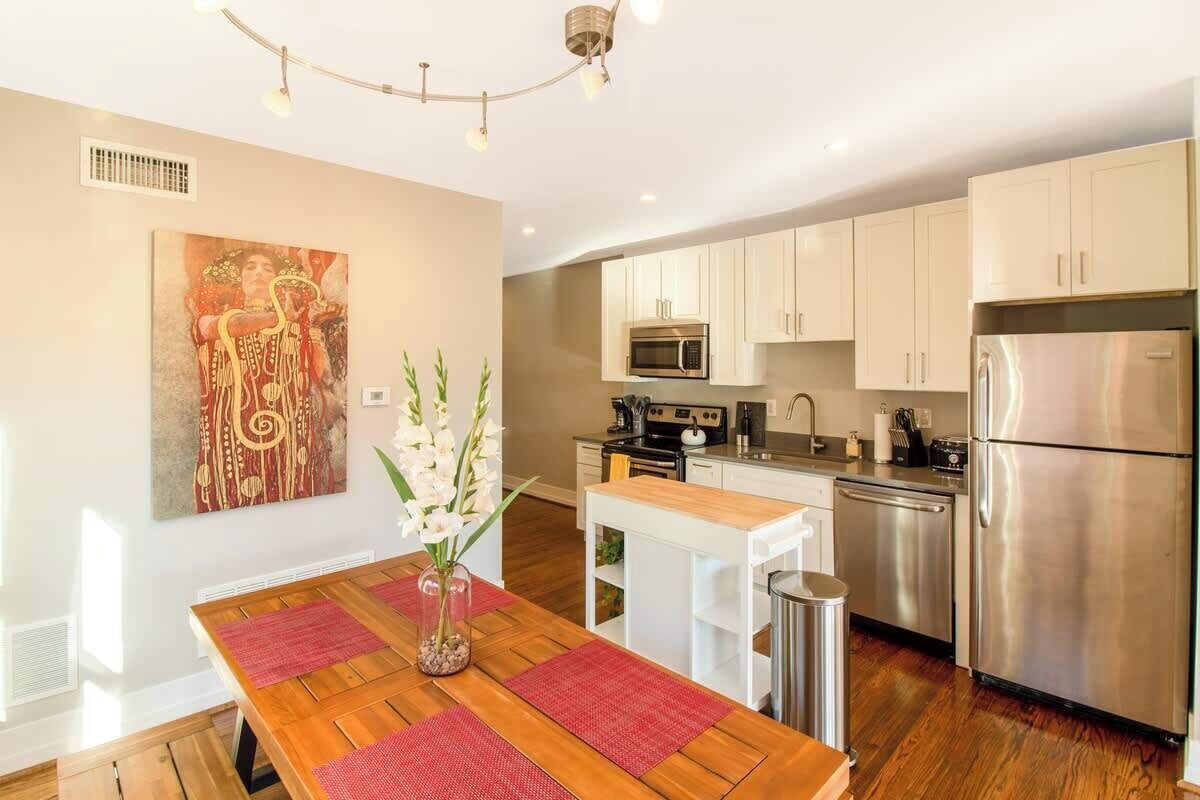 A modern kitchen with white cabinets, stainless steel appliances, and a wooden dining table with red placemats.