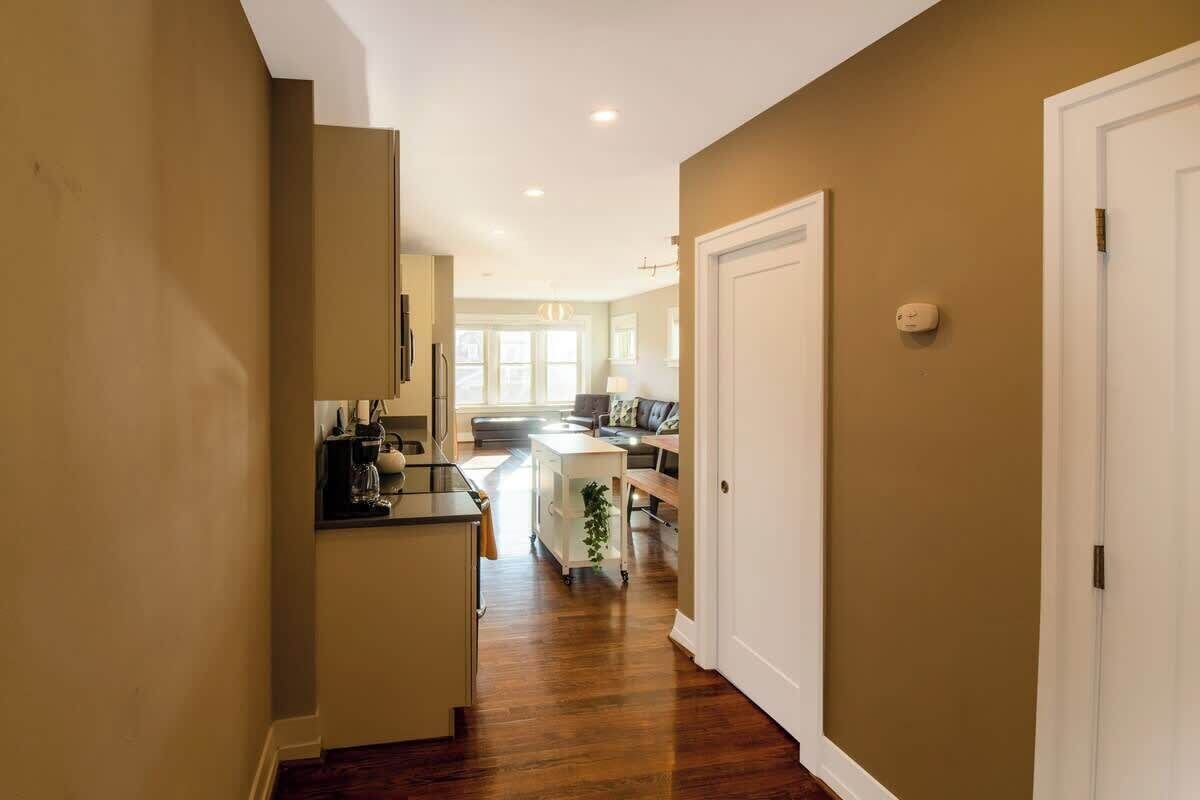 A hallway with a kitchen area, a dining table, and a sofa.
