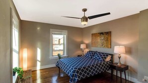 A bedroom with a bed, two bedside lamps, a ceiling fan, a window, and a wall-mounted artwork. - Chic Minimalist Gem w/ Fenced Backyard + W/D (Saint Louis)