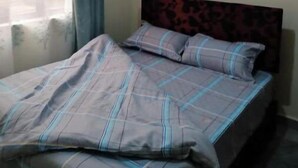 A bedroom with a bed, a headboard, and a window with curtains. - Exquisite City Apartments with hot tub (Nairobi)