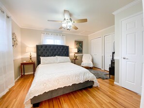 A bedroom with a tufted headboard, a large bed with a white bedspread, a ceiling fan, a window with sheer curtains, a painting on the wall, a white chair, and a wardrobe. - Family & Pet friendly home with HOT TUB! near Broadmoor and OCC!  (Colorado Springs)