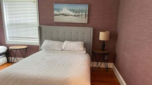 Una camera da letto con un letto, un comodino, una lampada, un quadro e una finestra con persiane.