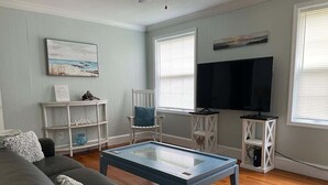 Un soggiorno con un divano grigio, un tavolino da caffè in vetro, un comodino bianco, una televisione e un quadro appeso al muro.