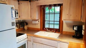 A compact kitchen with wooden cabinets, a white stove, a sink, and a window with a view of greenery outside. - Cottage Overlooking Paradise Lake (Carp Lake)