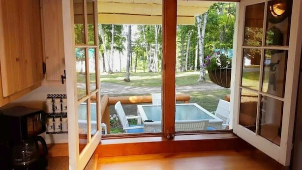 A room with a large sliding glass door leading to an outdoor patio with a hot tub and lounge chairs. - Cottage Overlooking Paradise Lake (Carp Lake)