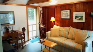 A cozy living room with a wooden wall, a striped sofa, a small table, and a lamp. - Cottage Overlooking Paradise Lake (Carp Lake)