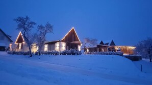 Un paisaje nevado con una casa de madera con techos triangulares iluminada por luces cálidas.
