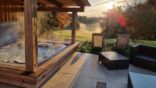 Un área de hidromasaje con terraza de madera, asientos al aire libre y una vista panorámica de colinas y árboles.