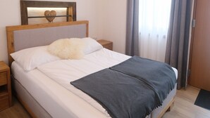 Una cama bien hecha con cabecera de madera, una mesita de noche y una ventana con cortinas.