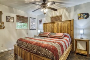 Een slaapkamer met een houten bed, een plafondventilator, een raam met zonwering en een poster aan de muur.
