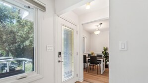 Un couloir avec une porte blanche, une porte vitrée dotée d’un portail en métal, et un coin repas avec une table et des chaises.