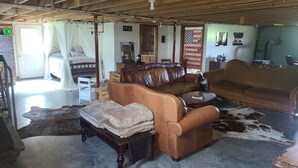 A spacious room with a large brown leather sofa, a wooden bed, and a cowhide rug. - The Bunkhouse @Dragonfly Ranch is made to make you feel like home away from home (Cub Run)