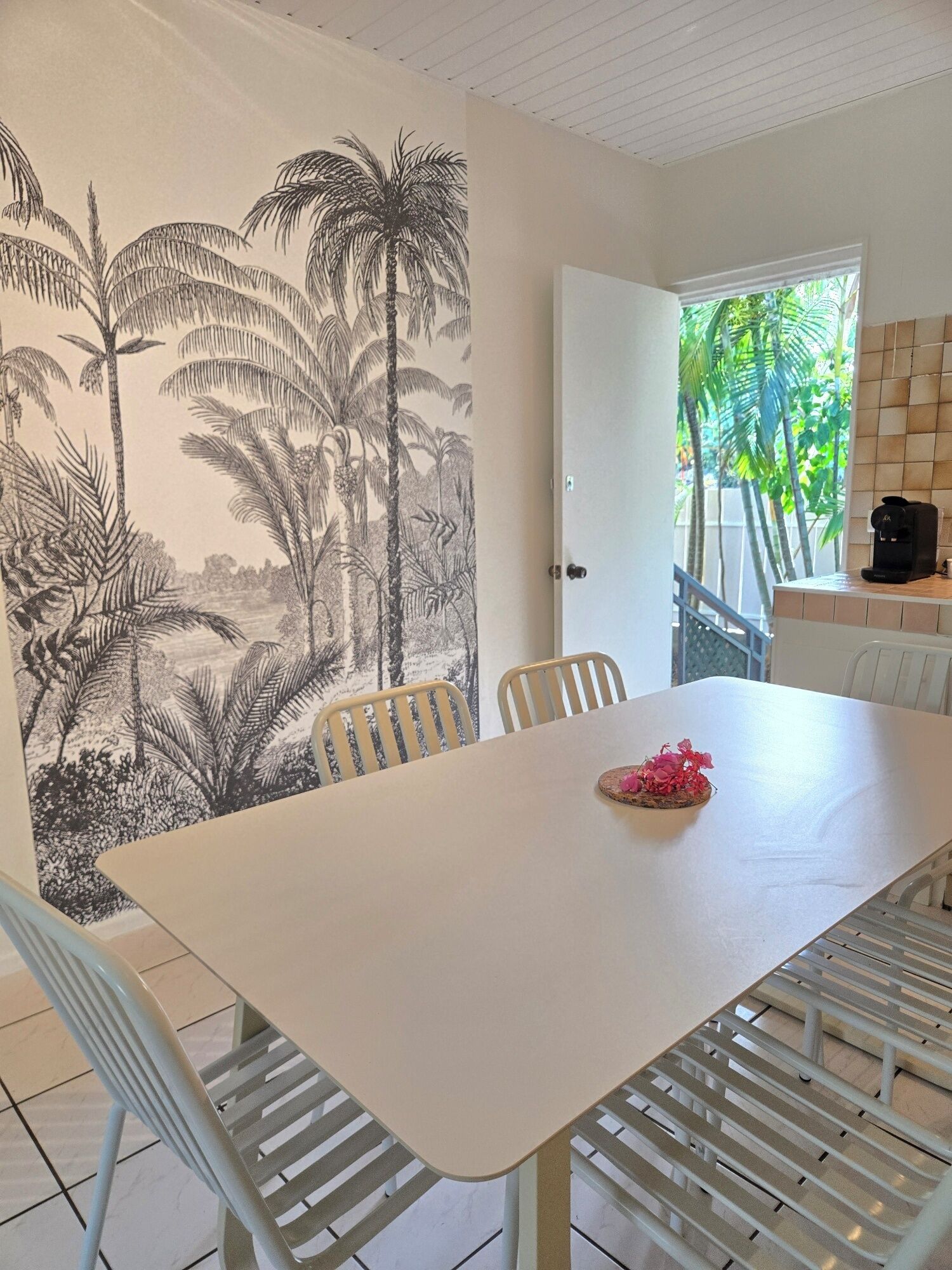 A dining area with a white table, chairs, and a mural of tropical foliage on the wall.