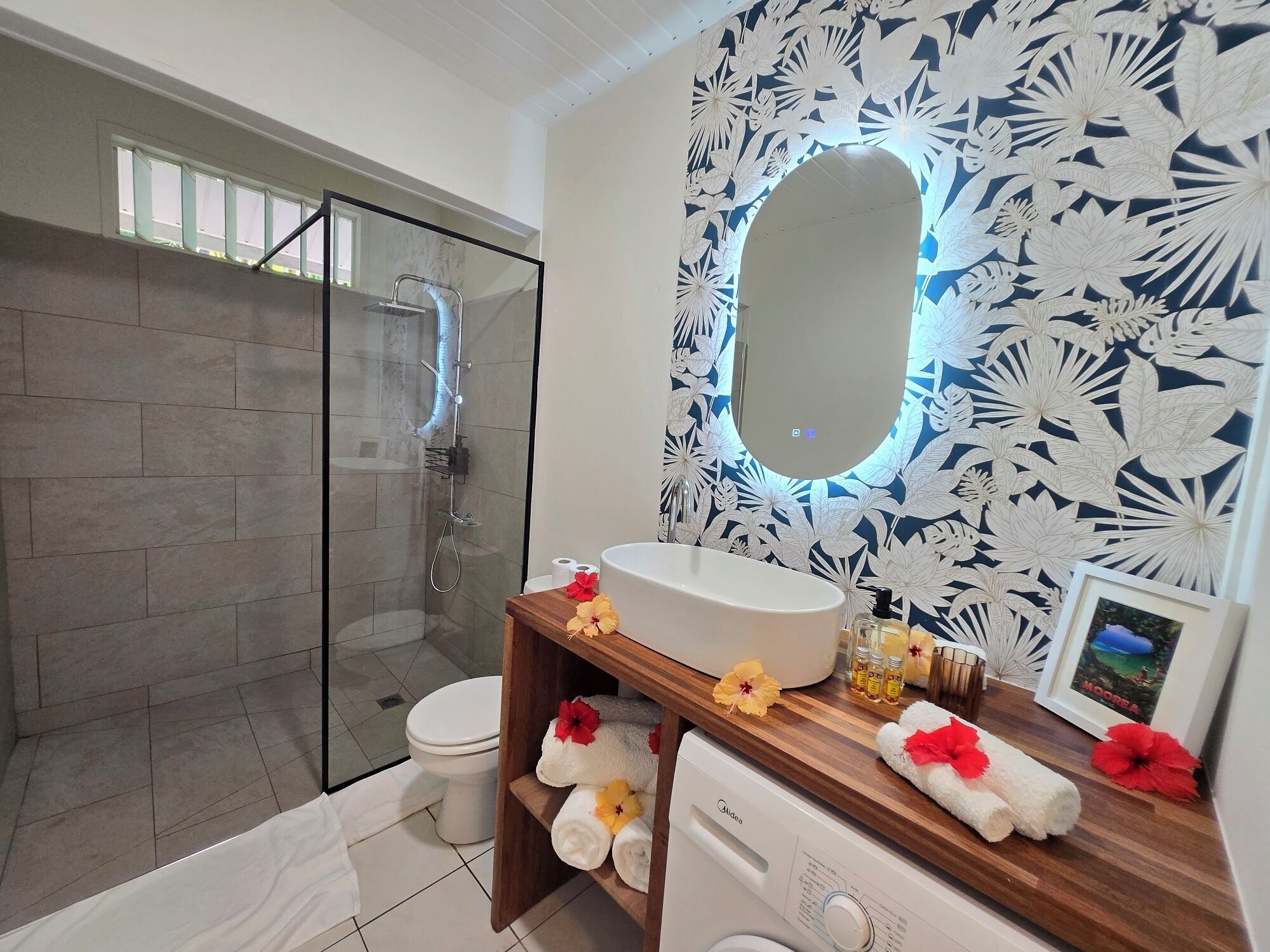 A bathroom with a glass shower enclosure, a white toilet, a wooden vanity with a sink, and a mirror.