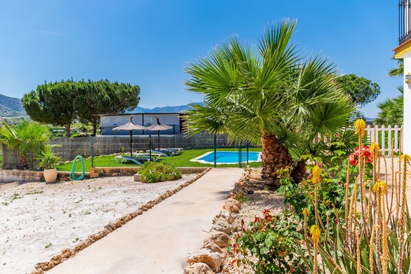 A pool area with a clear view of the mountains, a pathway, and a fenced garden with various plants.