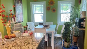 A kitchen with a granite countertop, white dining table, and chairs. There are decorative wall flowers and a potted plant.