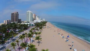 Una playa con palmeras, un paseo marítimo y edificios altos al fondo.
