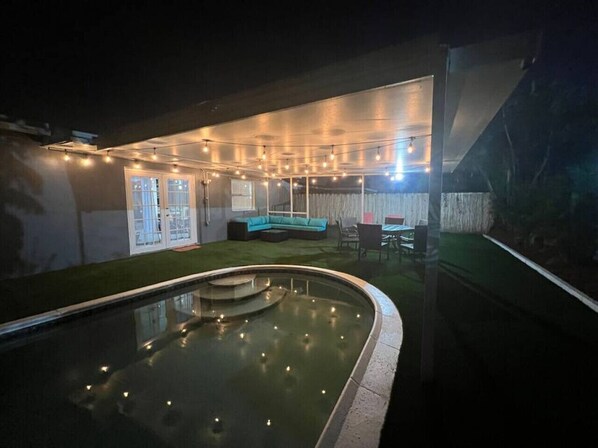 Une piscine dotée d’un espace détente intégré et illuminée de guirlandes lumineuses.