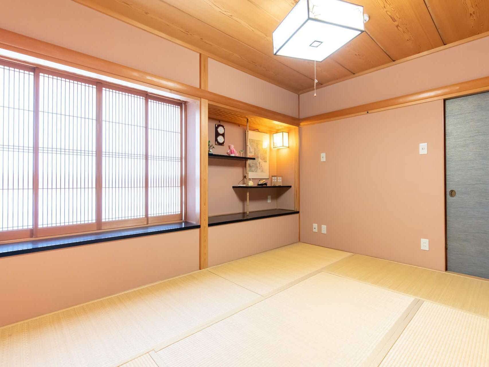 Perinteinen japanilainen huone, jossa on tatamimatto, shoji-tyylinen ikkuna, pieni hylly koriste-esineille ja liukuovi.
