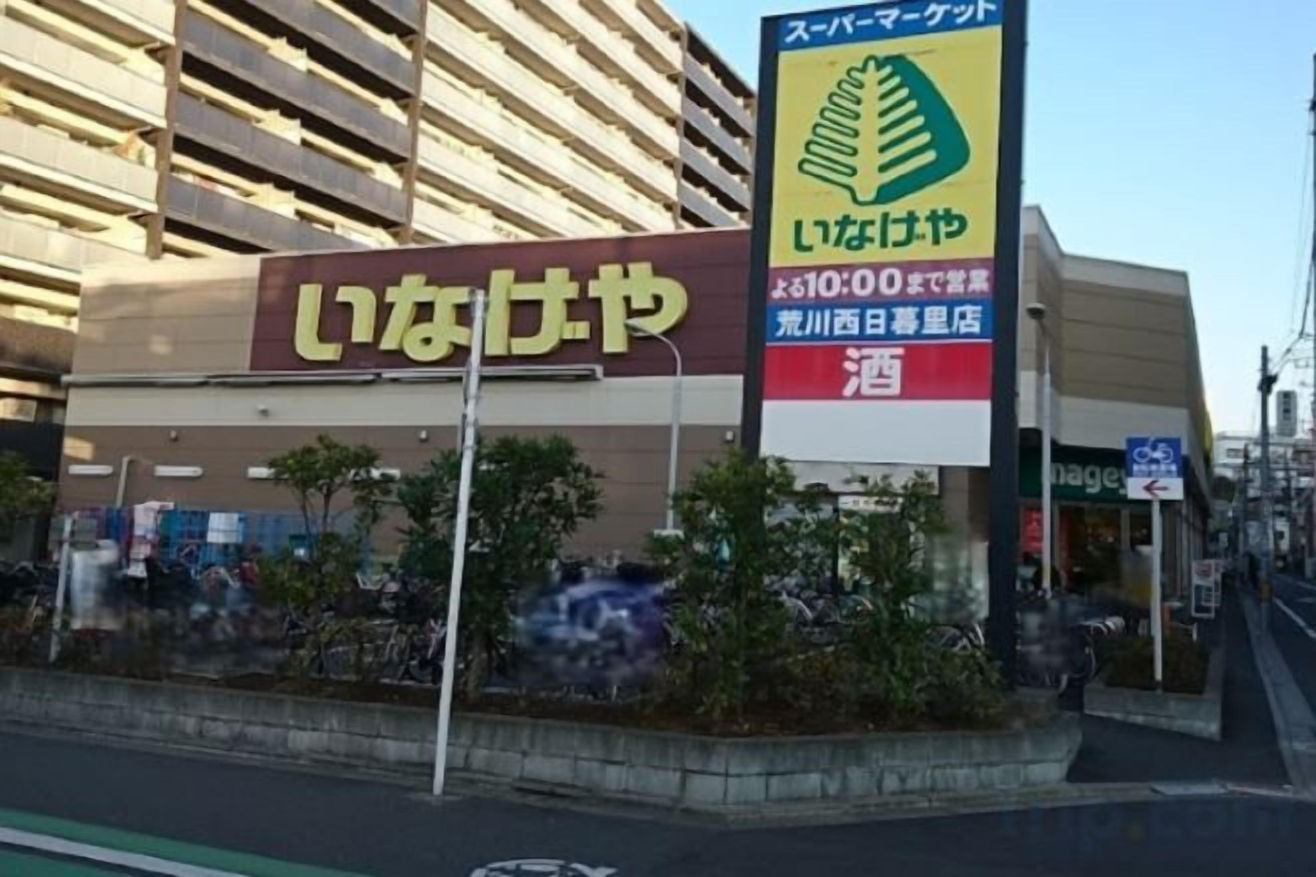 Un edificio con un cartello che riporta la scritta 'いなげや' e un altro cartello pubblicitario per un servizio.