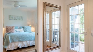 Un dormitorio con cama, ventilador de techo, espejo grande y ventana.