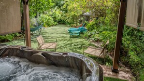 Un jacuzzi en un jardín exuberante con una pérgola, sillas y una hamaca.