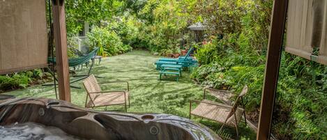 Un jacuzzi en un jardín exuberante con una pérgola, sillas y una hamaca.