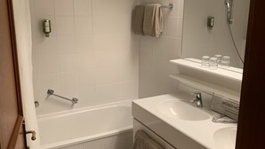 A modern bathroom with a bathtub, a sink, and a toilet. There are towels hanging on the wall and a showerhead above the sink. - Family apartment in the middle of Bad Gastein (Bad Gastein)