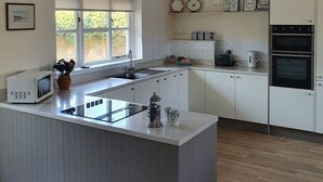 A modern kitchen with white cabinetry, a central island, a built-in oven, and a window providing natural light.
