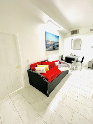A modern living room with a red sofa, a dining table with chairs, and a large mirror on the wall.